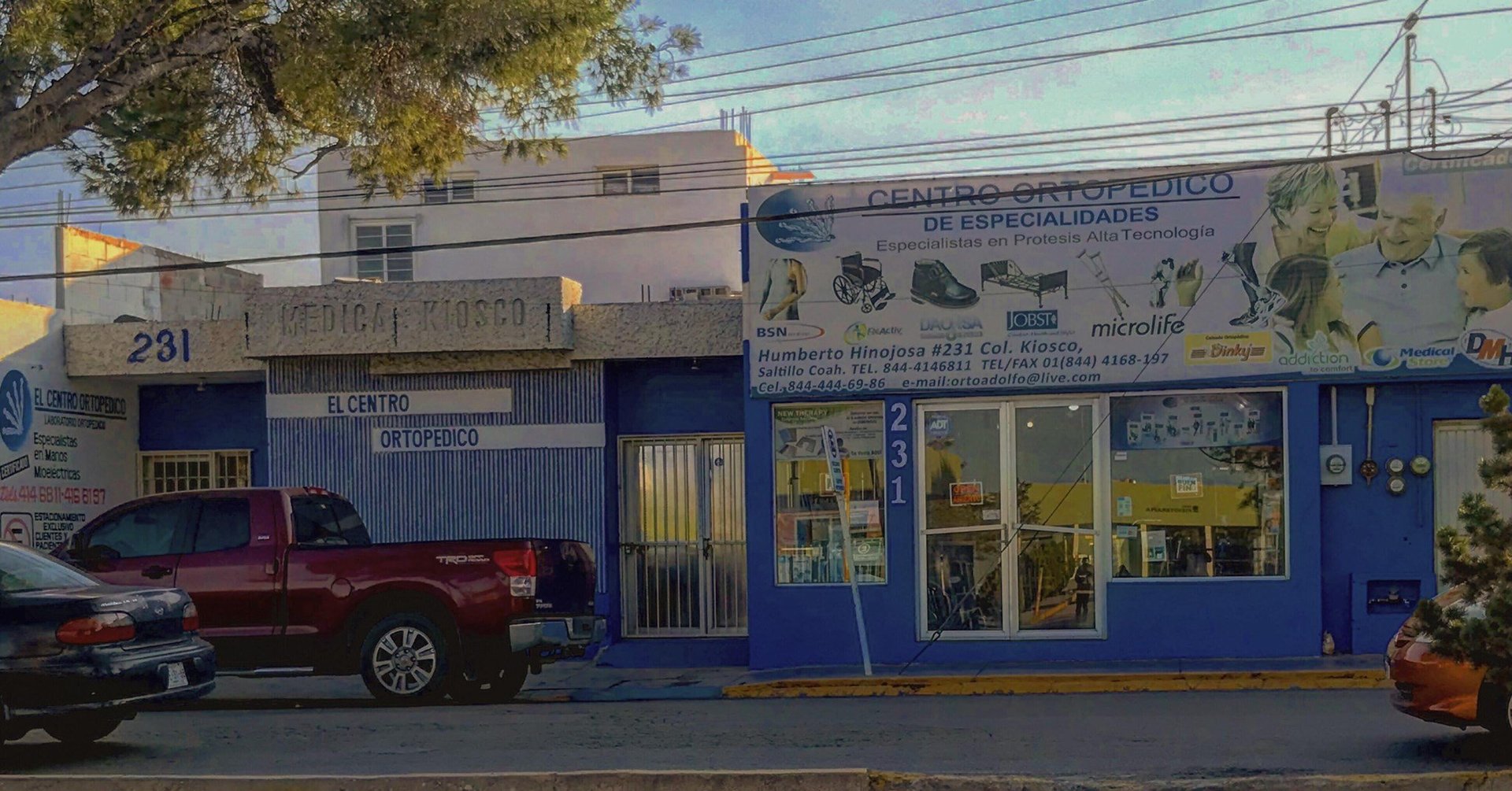 Blue storefront with yellow signage on street corner, parked red truck visible, overhead power lines